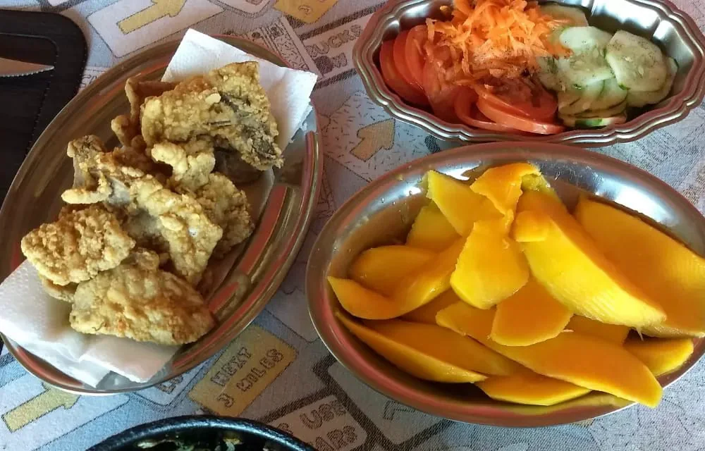 Prato servido: peixe frito, salada de tomate e pepino, manga fatiada e caldo verde com ovo